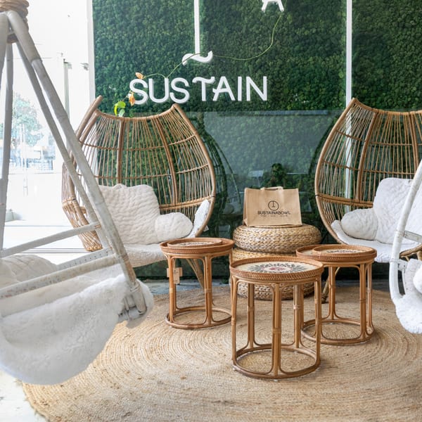 Sustainabowl restaurant interior with wicker chairs, small tables, and a moss wall with the "SUSTAIN" logo.