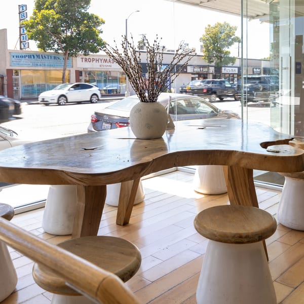 A large, live-edge wooden table with a vase of pussy willows, seen from inside a restaurant.
