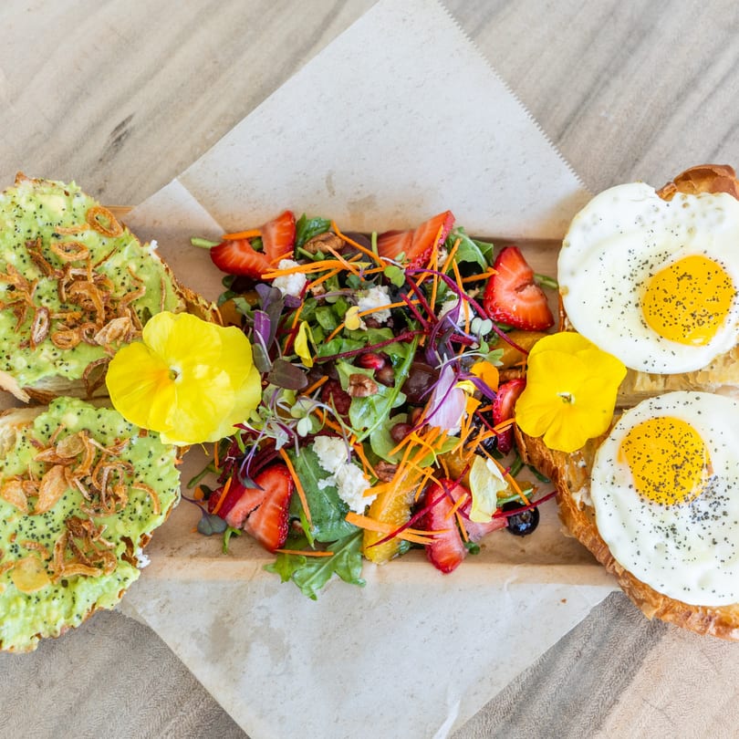 Avocado toast with fried onions, a colorful salad with strawberries, and two fried eggs on toast.