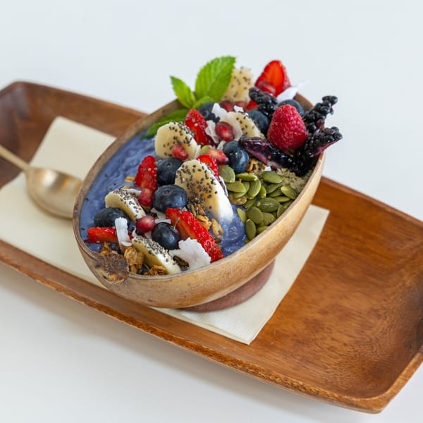 A vibrant blue smoothie bowl in a coconut shell, topped with fresh berries, banana, seeds, and mint.