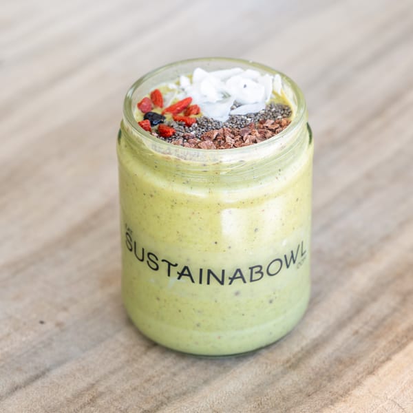 A Sustainabowl smoothie in a glass jar, topped with coconut flakes, goji berries, chia seeds, and cacao nibs.