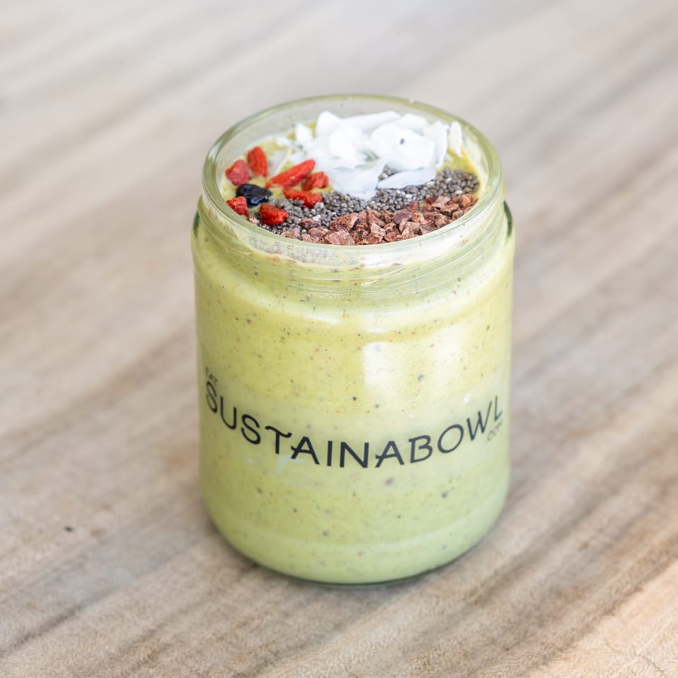 A Sustainabowl smoothie in a glass jar, topped with coconut flakes, goji berries, chia seeds, and cacao nibs.