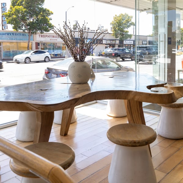 A unique wooden table with a vase of pussy willows, stools, and a street view outside.