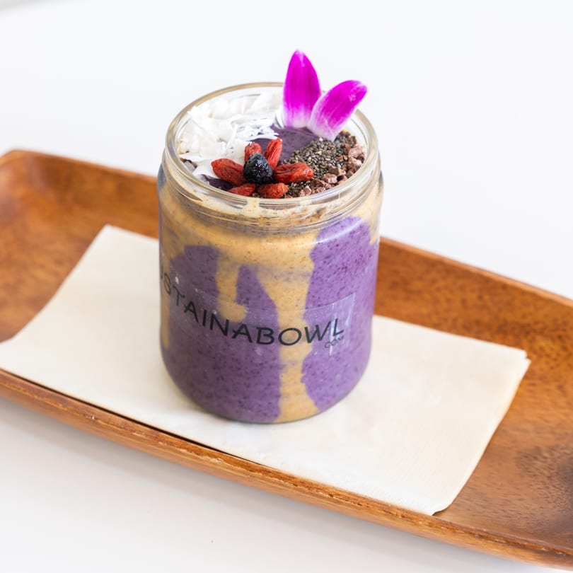 Purple smoothie with peanut butter swirls, topped with berries, coconut, chia seeds, and an orchid.