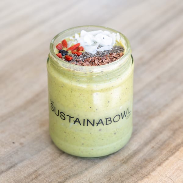 Green smoothie in a Sustainabowl jar, topped with coconut flakes, chia seeds, goji berries, and cacao nibs.