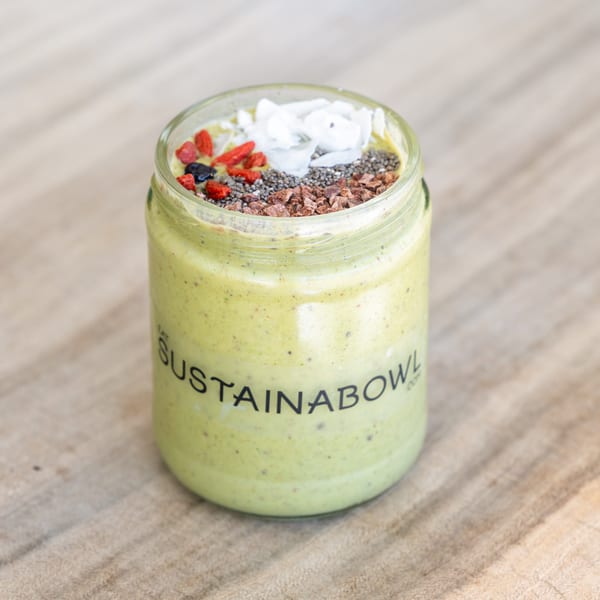 Green smoothie in a Sustainabowl jar, topped with goji berries, chia seeds, cacao nibs, and coconut flakes.