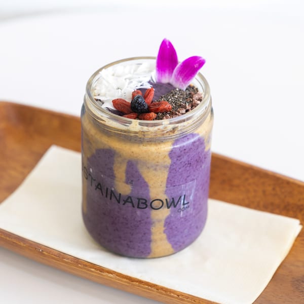 A purple smoothie with peanut butter swirls, topped with coconut, berries, chia seeds, and a flower.