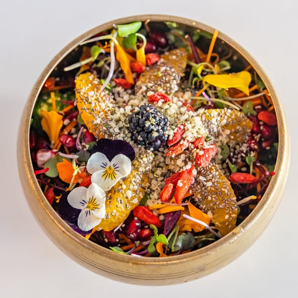 A Sustainabowl healthy bowl with fruit, seeds, microgreens, and edible flowers in a golden bowl.