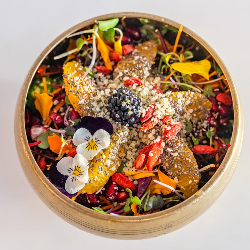 A Sustainabowl healthy bowl with fruit, seeds, microgreens, and edible flowers in a golden bowl.