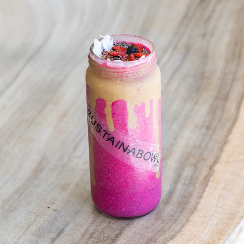 A Sustainabowl smoothie with pink and tan layers, topped with goji berries and coconut flakes.