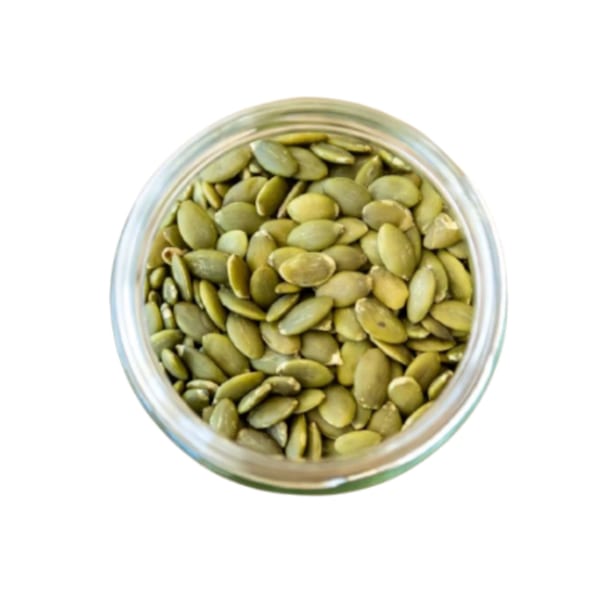 Overhead view of a glass jar filled with green pumpkin seeds, a healthy topping at Sustainabowl.