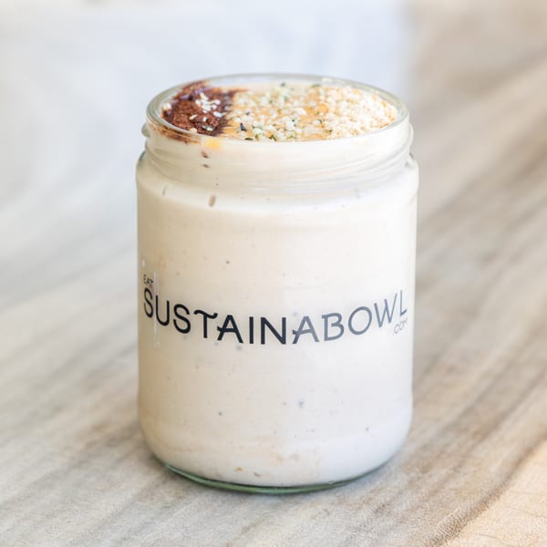A Sustainabowl smoothie in a glass jar, topped with cocoa powder, seeds, and honey.