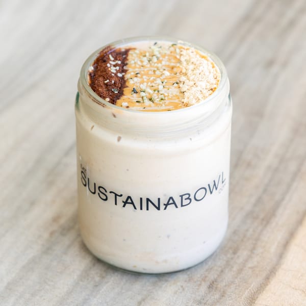 A Sustainabowl smoothie in a glass jar, topped with chocolate, peanut butter, and seeds.