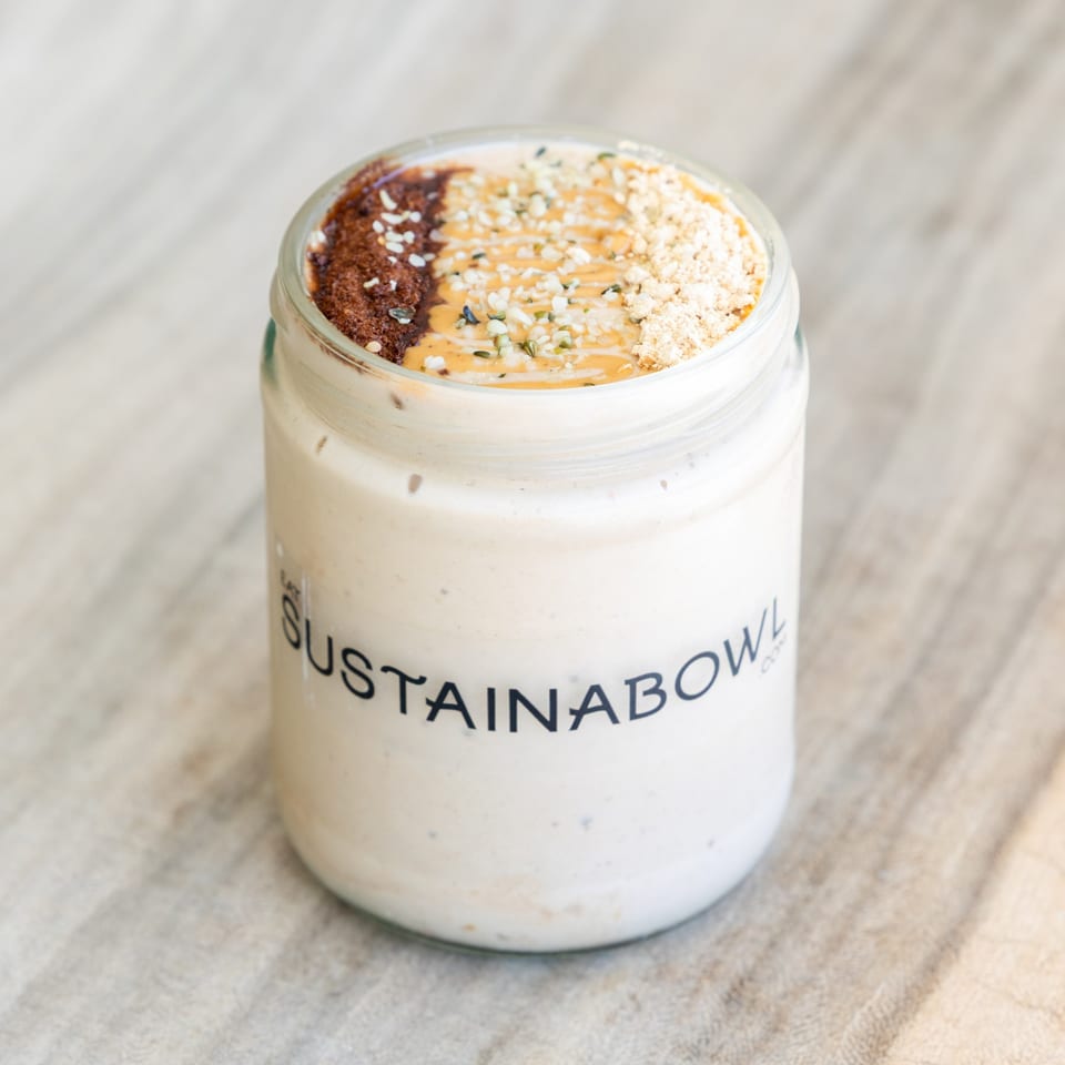 A Sustainabowl smoothie in a glass jar, topped with chocolate, peanut butter, and seeds.