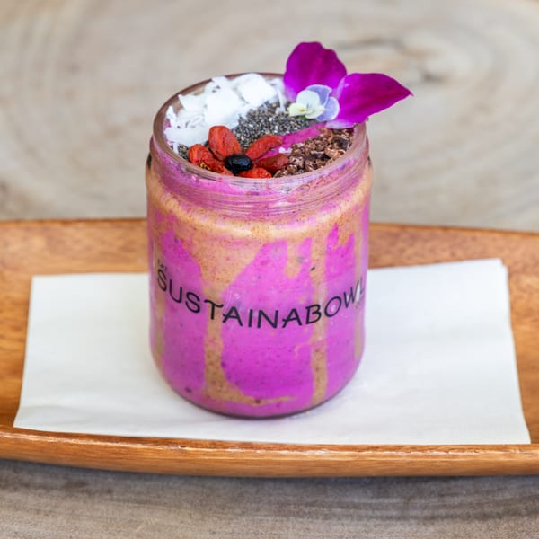 Sustainabowl smoothie in a glass jar, topped with coconut, chia seeds, goji berries, and an orchid.