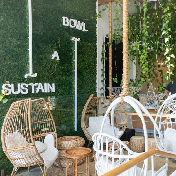 Cozy restaurant interior with wicker chairs, tables, green moss wall, and hanging plants.
