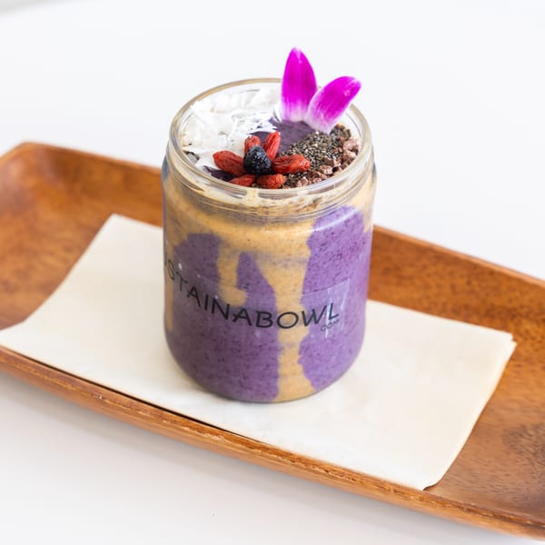A purple smoothie with peanut butter swirls, topped with berries, coconut, chia seeds, and a pink orchid.