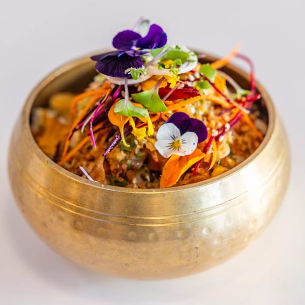 A Sustainabowl healthy bowl with colorful vegetables and edible flowers in a golden bowl.