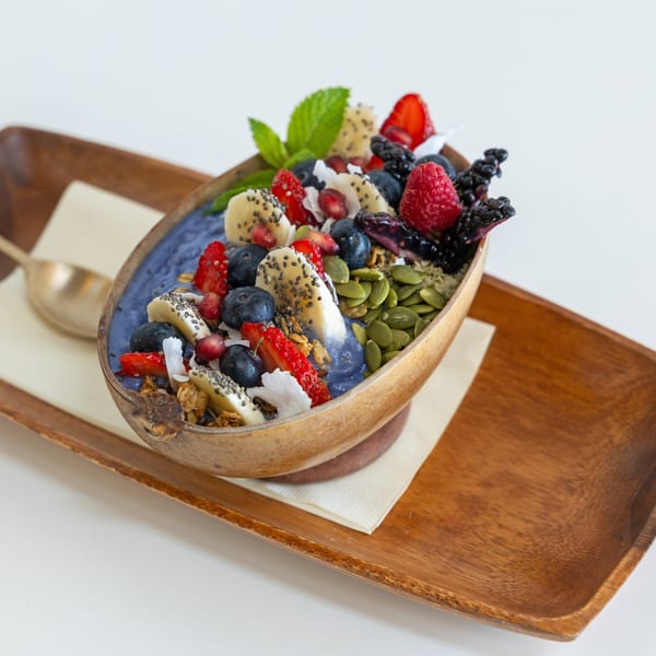 A vibrant blue smoothie bowl in a wooden bowl, topped with fresh berries, banana, granola, and seeds.