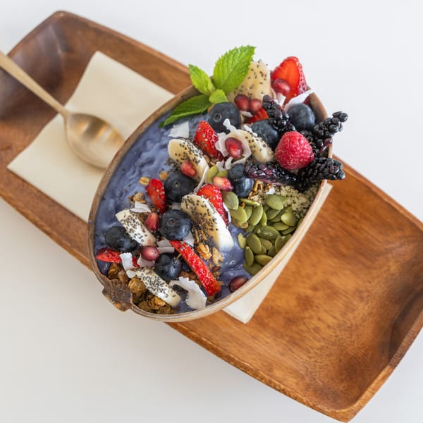 A vibrant smoothie bowl with berries, banana, granola, and seeds, served on a wooden tray.