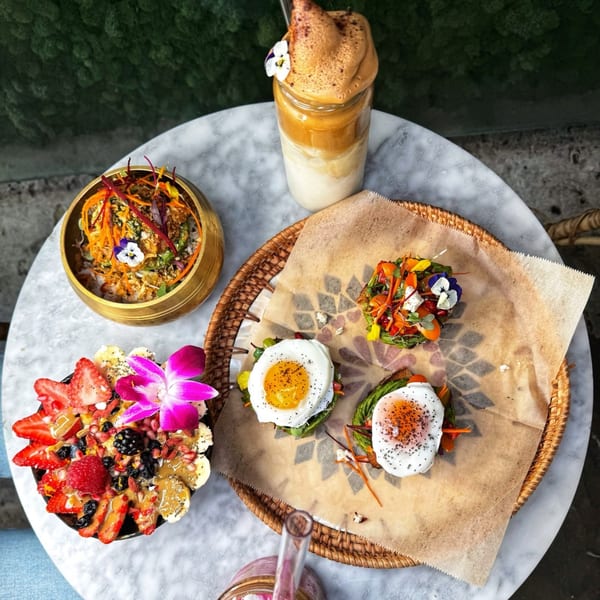 Overhead view of a marble table with a smoothie, a colorful salad, an acai bowl, and avocado toasts.