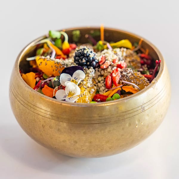 A Sustainabowl healthy fruit bowl in a brass bowl, topped with berries, seeds, and edible flowers.