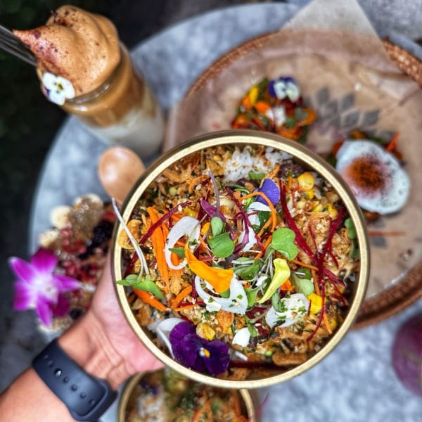 Overhead view of a hand holding a colorful salad bowl with edible flowers, surrounded by other dishes.