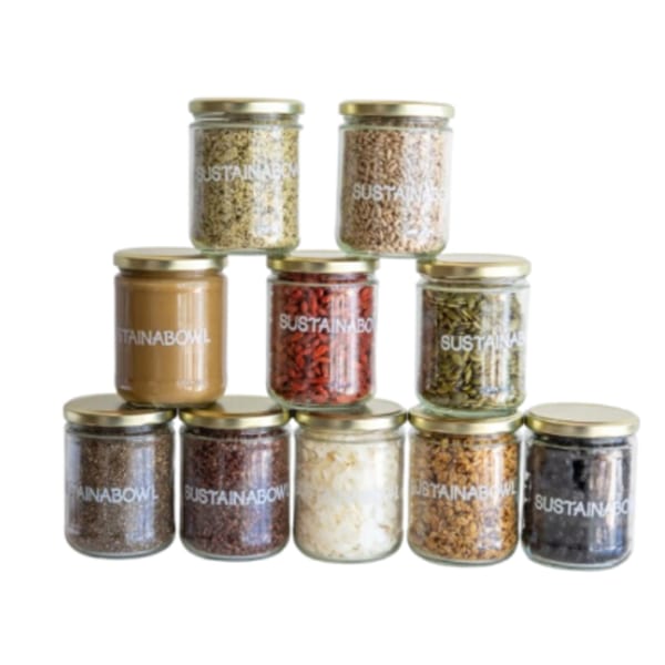 A pyramid of Sustainabowl jars filled with various healthy toppings like seeds, nuts, and dried fruit.