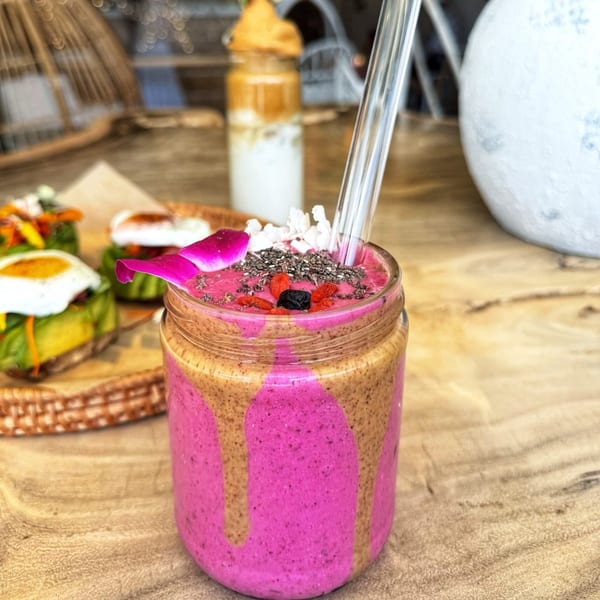 Pink and brown layered smoothie with chia seeds, goji berries, and a flower petal.