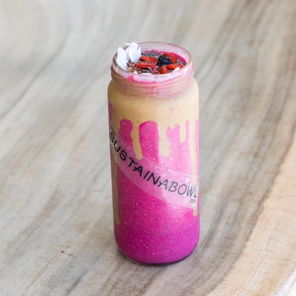 Sustainabowl smoothie in a glass jar with pink and tan layers, topped with berries and coconut flakes.